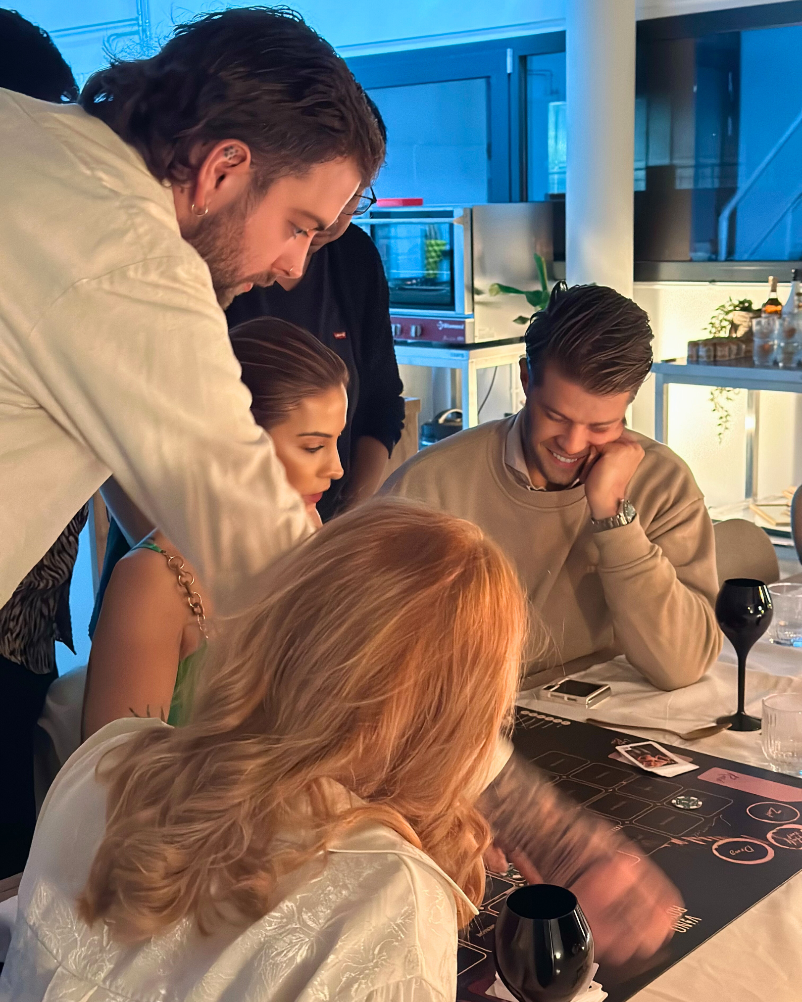 Ron van Noord — Visual design, Grafisch ontwerp, DTP, Visual design — Vino & Cerveza Royale — Beeld: Een groep deelnemers speelt samen rond het spelbord met karakterkaarten, roulettechips en zwarte proefglazen. — Project: Een spel vol smaak, spanning en karakter.
