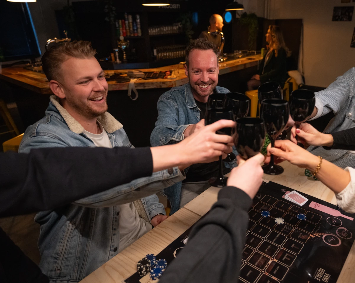 Ron van Noord — Visual design, Grafisch ontwerp, DTP, Visual design — Vino & Cerveza Royale — Beeld: Deelnemers proosten met zwarte proefglazen boven het spelbord van Vino Royale. — Project: Een spel vol smaak, spanning en karakter.